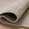 Rolled edge of Polly Smoke/Sand rug on hardwood floor emphasizing pile thickness and texture.