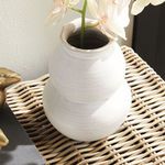 Vase with cream faux orchid stem viewed from a higher angle on a woven rattan surface beside decor