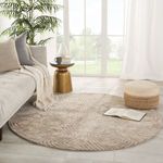 Round beige rug with hand-tufted labyrinth texture placed on light wood floor in a bright modern living room