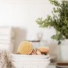 Stacked colanders filled with natural bristle brushes on a white shelf with plants and towels
