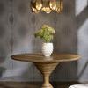 Ivory ceramic vase styled on round wooden pedestal table with green flowers indoors under gold pendant light.