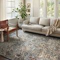Saban Blue/Sand rug styled in living room with beige sofa, wooden chair and sunlight from large windows