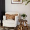 Indoor setting with two teak stools next to white textured armchair and potted plant on larger stool