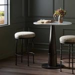 Two Corinne Stools with boucle seats paired with pedestal table in dark green paneled room