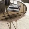 Close-up of Calliope Cocktail Table's metallic frame and smoked glass surface with decorative books and vase