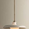 Pendant light hanging against beige wall with visible brass stem and wide off white shade