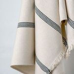 side view of throw hanging, showing fabric weight and diagonal black stripe detail with fringed border
