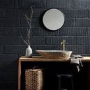 Stain grey/brown vase holding thin branches placed on wooden vanity with stone sink, black wall and round mirror