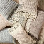 Group of different patterned lumbar pillows in neutral tones arranged on soft beige surface