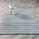 Del Mar area rug styled in a room setting under a small wooden stool on light herringbone wood floor