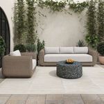 Outdoor side table used as coffee table in patio setting with cream-colored sofa and armchair surrounded by greenery