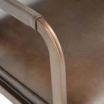 Close-up of bronze finish metal armrest and edges over brown leather seat