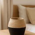 Black and natural bamboo flower vase on wooden surface with neutral pillows and curtains in background