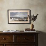 Painting hanging on wall above wooden dresser styled with books and a gold vase with dried flowers