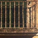 Close-up of rusted ornate wrought iron balcony railing casting shadow on beige wall above the door