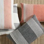 Group of pillows including black/cream striped and coral/cream striped designs on textured tan surface