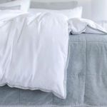 Shore blue coverlet under white duvet with light blue trim in a bright bedroom setting