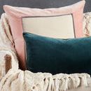 Teal lumbar pillow displayed on a cream chair with a pink and cream square pillow and cozy throw