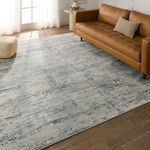 Isola rug laid in living room setting under brown leather sofa on wood floor with natural light from window