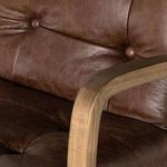 Tight close-up of ash wood armrest junction with button tufting on leather backrest.