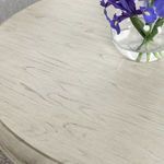 Close-up view of the tabletop’s light wood finish and visible natural grain with a vase of purple flowers