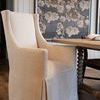 Three-quarter front view showing chair arm height and skirt pleats beside wooden dining table