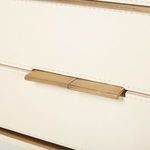 Close-up of two brass drawer handles on ivory leather front centered between stitching
