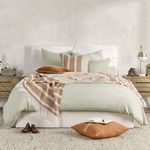 Styled bedroom with duvet, sage and rust striped throw blanket, and decorative pillows on bed