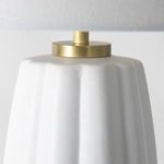 Close-up top of white lamp body showing subtle textured ceramic surface and gold metal hardware