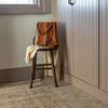 Heritage Clay rug placed in entryway setting with herringbone tile, small wooden chair, tan leather bag, and cream scarf