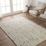 Rug shown styled in a bright room with natural wood floor and light beige armchairs