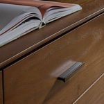 Close-up of a wooden dresser drawer with metal handle and an open book resting on top