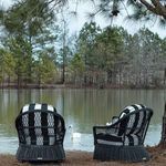 Two outdoor wicker swivel chairs with striped cushions facing lake under trees