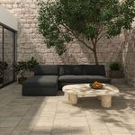 Outdoor setting with sectional positioned on tiled patio in front of limestone wall and leafy tree
