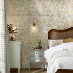 Bedroom setting showing Rosamund wallpaper on walls behind rattan bed and pale green furniture
