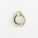 Close-up of antique brass ring drawer pull mounted on white textured linen drawer front