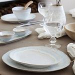 Oval platter styled on wooden table with matching bowls, glasses, and folded napkins in neutral setting