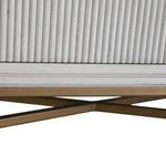 Close view of crossed brass base supports beneath the chest with matte metallic finish