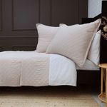 Monaco Coverlet in a soft beige tone with diamond quilted pattern and matching pillows on a dark wood bed frame