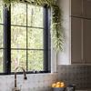 Kitchen sink area showing daisy-shaped planter beside bowl with oranges under a window with hanging leafy garland