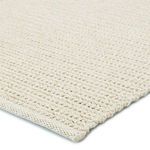 Close-up of braided polypropylene fibers showing tightly woven texture and edges of beige and ivory rug