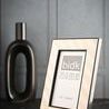 Picture frame displayed on black surface with gray paneled wall and black vase in background