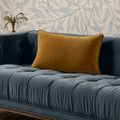 Gold-toned velvet pillow styled on a tufted blue velvet sofa with patterned wallpaper background