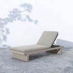 Leroy chaise shown outdoors on textured stone flooring with shadow of tree branches on wall behind