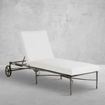 Outdoor armless chaise lounge with white cushion and dark wrought aluminum frame featuring subtle gold accents