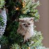 Side view of one owl sculpture perched on a decorated Christmas tree with metallic and textured baubles