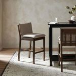 Wilmington Stool placed next to a black dining table in a minimalistic room with beige walls and a patterned rug