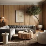 Sectional in a styled room with wood paneled walls, potted tree, round wood coffee table, and rug