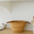 Bamboo basket on wooden countertop with kitchen bowls and utensils in background