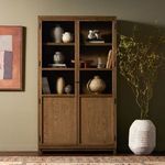 Softly lit styled setting showing cabinet with open glass door, ceramics, and plants